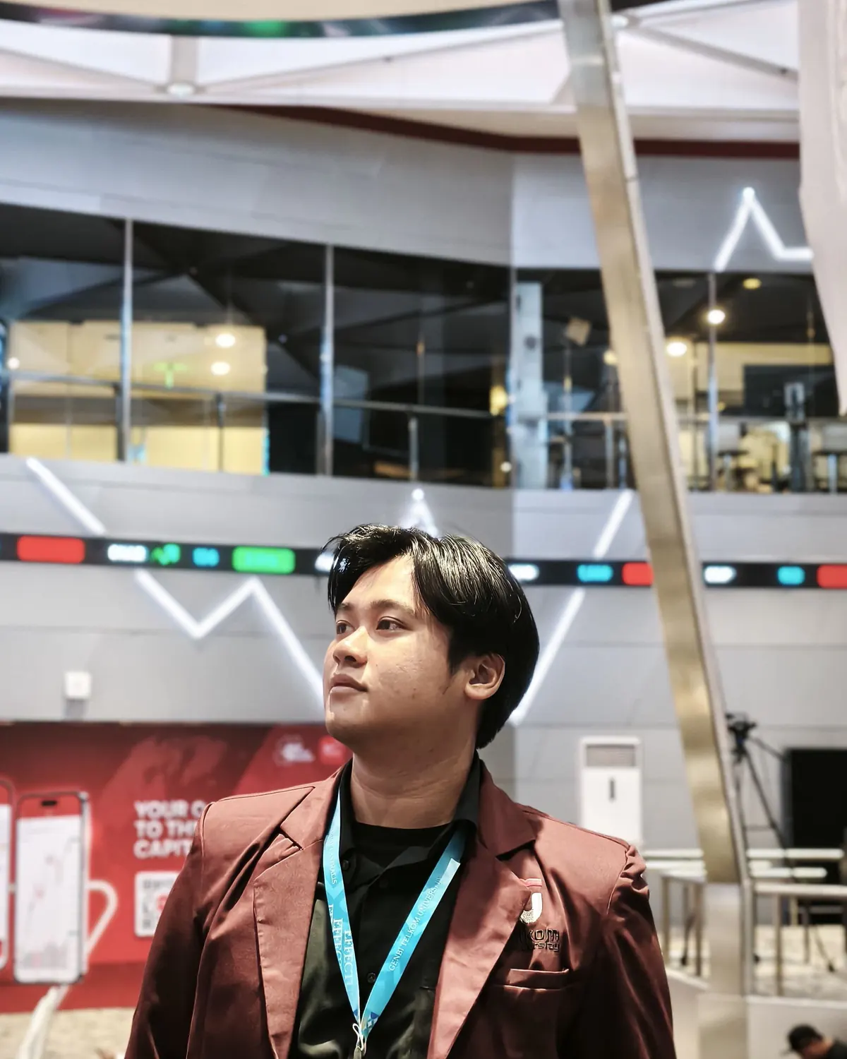 Wildan wearing a maroon jacket and event lanyard in an indoor venue.