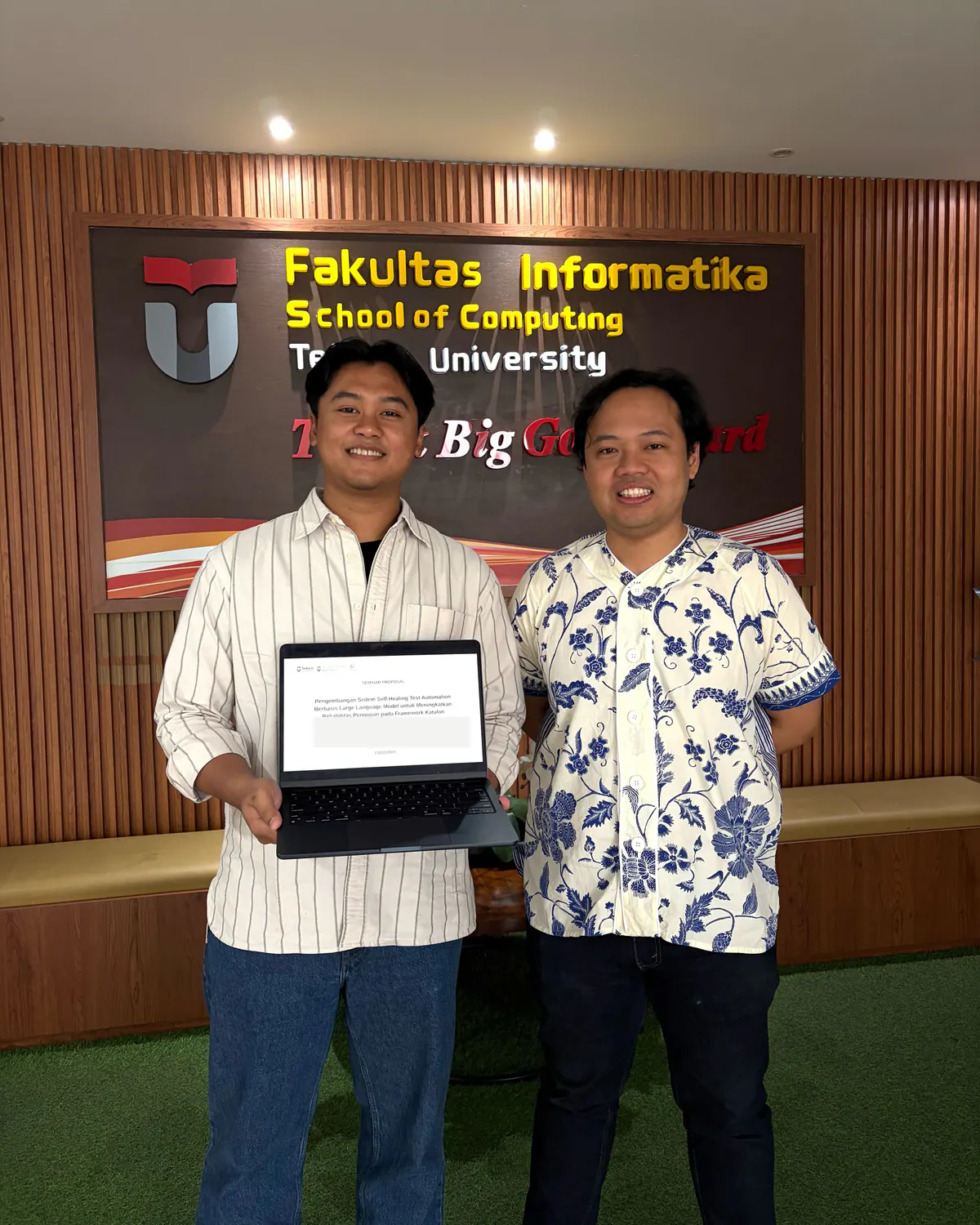 Wildan stands with a colleague while holding a research proposal document at the School of Computing.